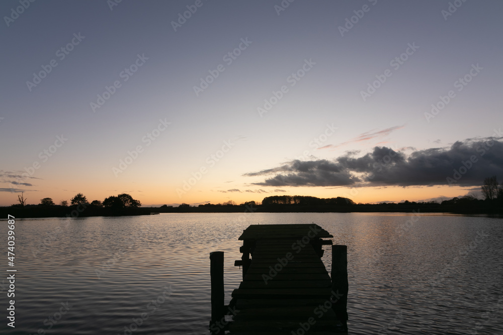 Silhouette of a wooden jetty by the lake after sunset at dawn.