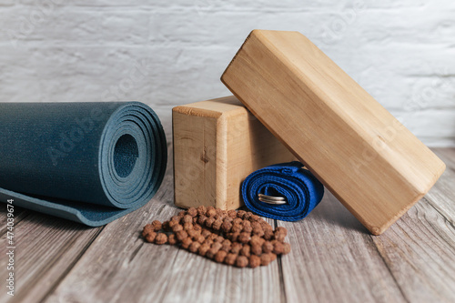 Closeup of two wooden yoga blocks, belt, rudraksha rosary and blue yoga mat on the wooden floor. Fitness, stretching and relaxation.