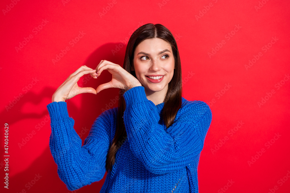 Photo portrait brunette in stylish pullover showing heart looking empty space isolated vibrant red color background Photo portrait brunette in stylish pullover showing heart looking empty space isolated vibrant red color background