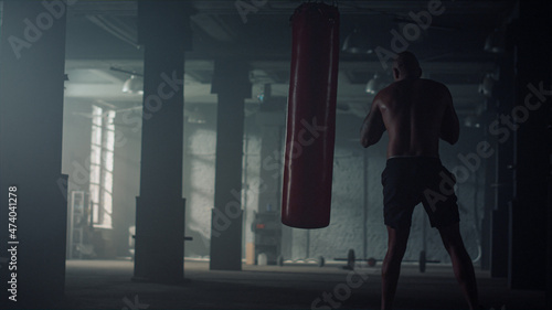 Muscular man boxing punch bag. Male boxer doing cardio workout in sports club
