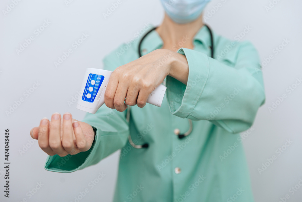 Temperature measurement gun in doctor hands. Close-up shot of doctor wearing protective surgical mask ready to use infrared isometric thermometer gun to check body temperature for virus symptoms. Temperature measurement gun in doctor hands. Close-up shot of doctor wearing protective surgical mask ready to use infrared isometric thermometer gun to check body temperature for virus symptoms.