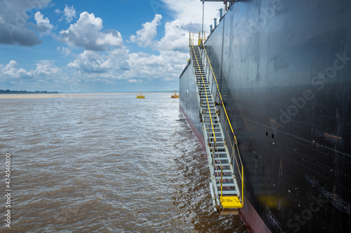 Beautiful view of black cargo ship and access ladder on sunny summer day with clouds on Amazon river. Manaus, Amazonas, Brazil. Concept of environment, ecology, nature, vessel, travel, transport. © Imago Photo