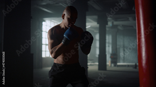 Boxer practicing kicks on punching bag in gym. Guy boxing sports bag in gloves