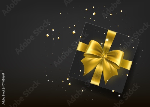 Black gift box with ribbon and gold bow, top view.
