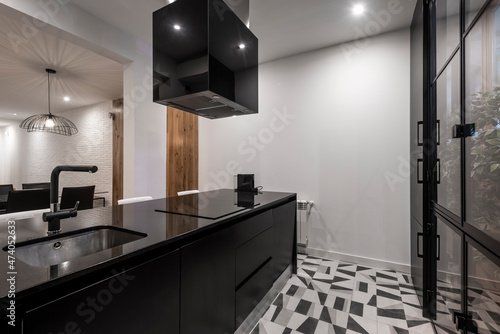 island and kitchen cabinet with black appliances next to a window with plants in a vacation rental apartment