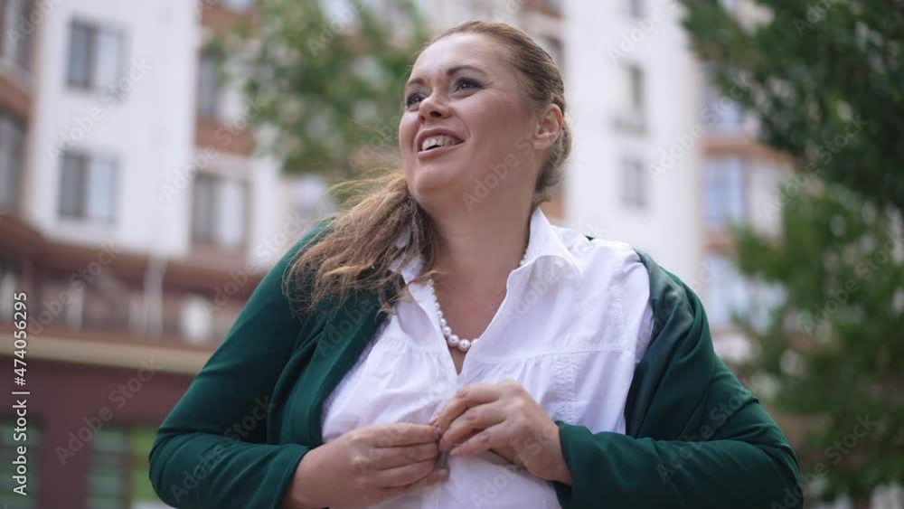 Happy smiling beautiful Caucasian plus-size woman buttoning shirt in slow motion walking away. Portrait of satisfied confident obese businesswoman leaving on city street outdoors Happy smiling beautiful Caucasian plus-size woman buttoning shirt in slow motion walking away. Portrait of satisfied confident obese businesswoman leaving on city street outdoors