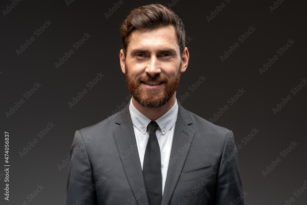 Portrait of happy good looking businessman in formal suit smiling to the camera in front of black wall background. Stock photo Portrait of happy good looking businessman in formal suit smiling to the camera in front of black wall background. Stock photo