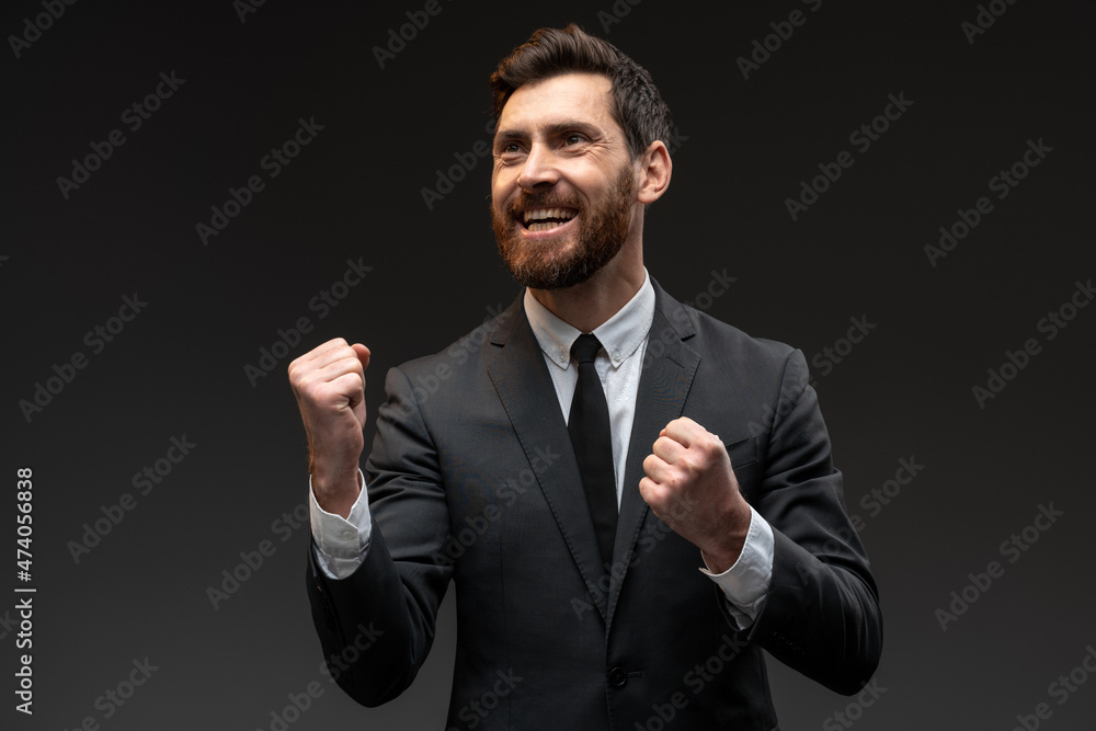 Portrait of happy screaming handsome bearded man in formal suit standing with excited face and rejoicing his victory. Indoor studio shot isolated on black background Portrait of happy screaming handsome bearded man in formal suit standing with excited face and rejoicing his victory. Indoor studio shot isolated on black background