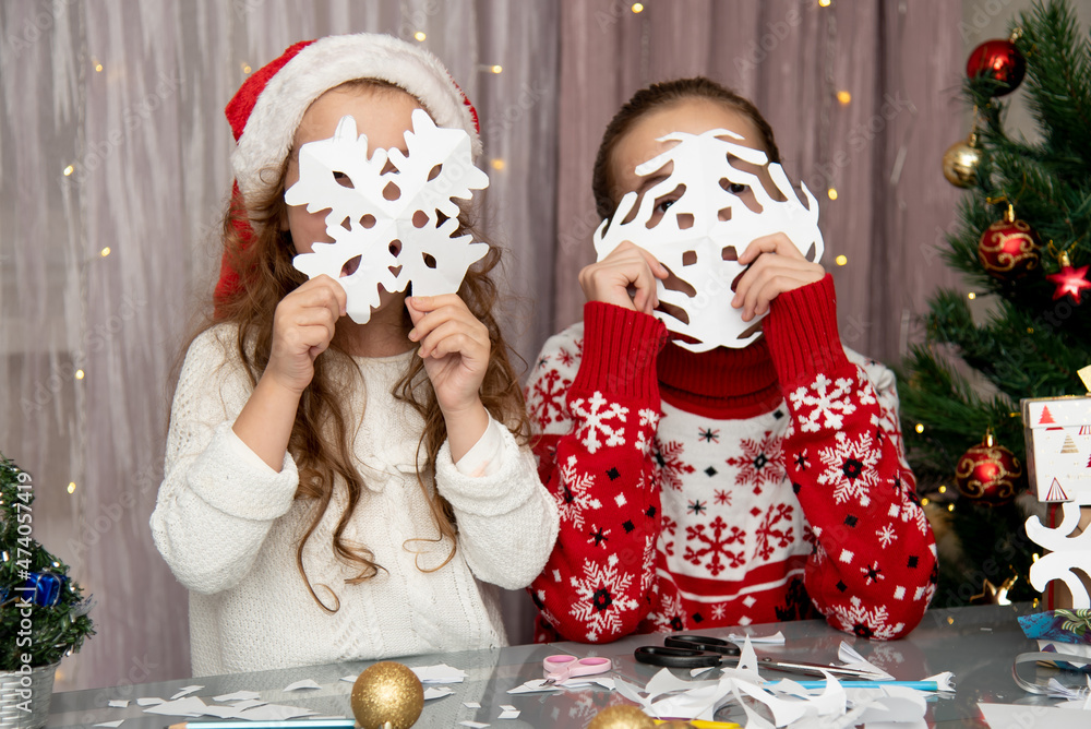 Two cute sisters cut snowflakes out of paper, preparing for the holiday. New Year. Christmas. Comfort.