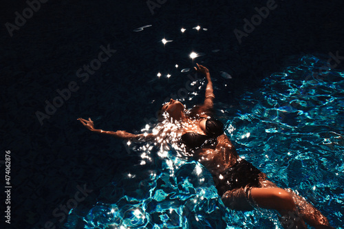 View from the top. Fashion portrait of a beautiful girl floating in the swimming pool in the turquoise water at the wellness resort.