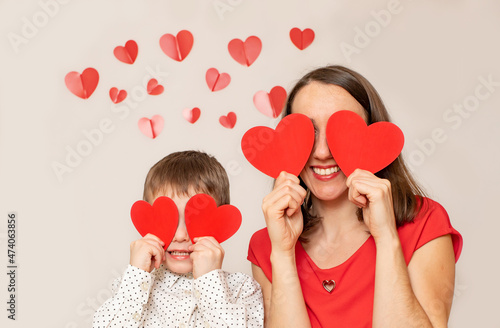 Mom and litl son are holding red paper hearts and smiling. Blonde caucasian people. Valentines day and love