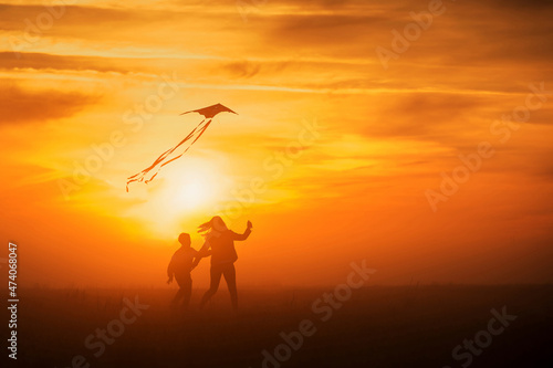 Flying a kite. Girl and boy fly a kite in the endless field. Bright sunset. Silhouettes of people against the sky. © Olga