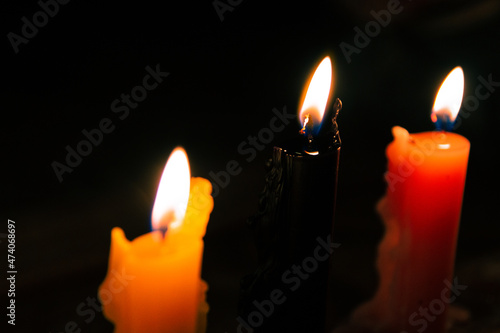 Close up of a black candle on row of lit colored candles on a windy night.
