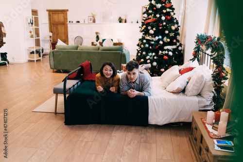 Couple lying on bed near christmas tree at home