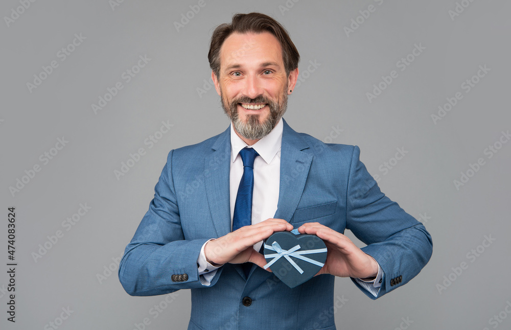 happy senior man in suit hold heart gift box on grey background, mens day