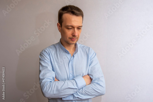 Portrait of a 30-35-year-old man in a blue shirt with crossed arms, stands on a light background. Perhaps he is a lawyer or a lawyer, a coach or a psychologist.
