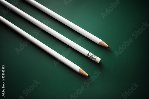 Three blank white pencils on green background.