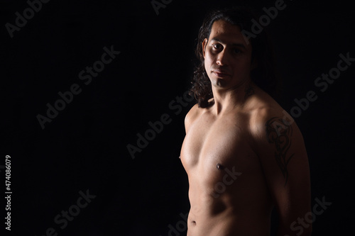  low key portrait of a man with tattoo looking at camera and serious on black background