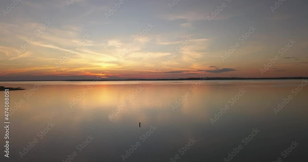 Beautiful sunset over the lake. View of the fisherman silhouette in the distance. Blue sky and orange clouds. Beautiful sunset over the lake. View of the fisherman silhouette in the distance. Blue sky and orange clouds.