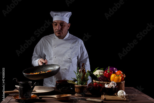 Male chef in white uniform holding a frying pan with fresh vegetables
