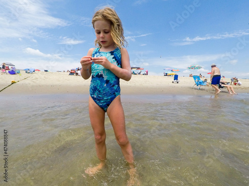 little girl in ocean holding something and looking at hands photo