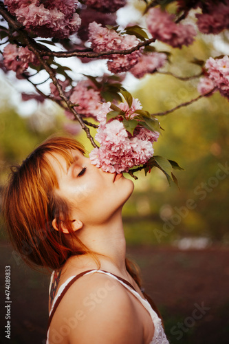 red-haired girl with fringe sniffs the flowers of a blooming tree