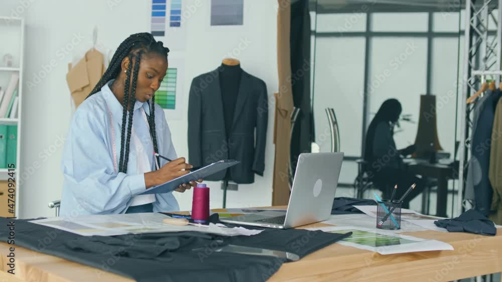 Successful Businessman-tailor, African-American Girl, Works with Sketches of Clothes, Using a Laptop. Creation of an Individual Costume in a Luxurious Atelier. Sewing Small Business, Fashion Industry. Successful Businessman-tailor, African-American Girl, Works with Sketches of Clothes, Using a Laptop. Creation of an Individual Costume in a Luxurious Atelier. Sewing Small Business, Fashion Industry.