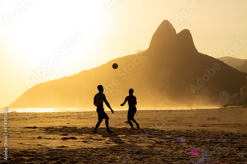 Two Brothers Mountain behind 2 friends playing soccer at Ipanema Beach, Rio de Janeiro. Sunset at summer photo