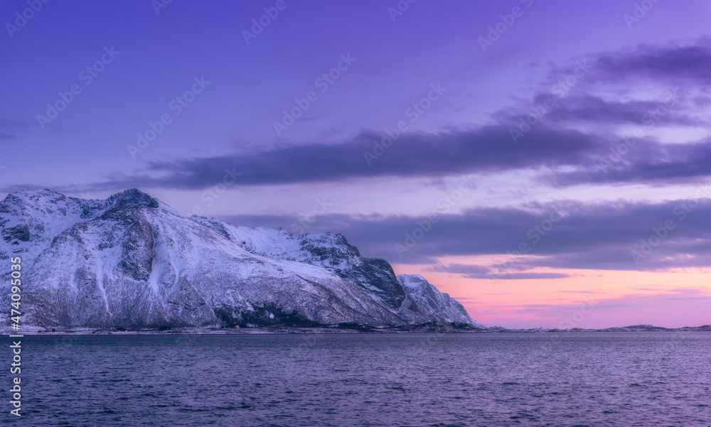Beautiful snow covered mountains and violet sky reflected in water at dusk. Winter landscape with sea, snowy rocks, purple sky, reflection, at sunset. Lofoten islands, Norway at twilight. Nature