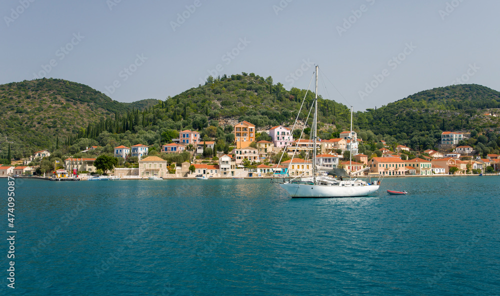 Panoram of the small town with multicolored houses on the hill with mountains on the background and a yacht sailing infront of the town