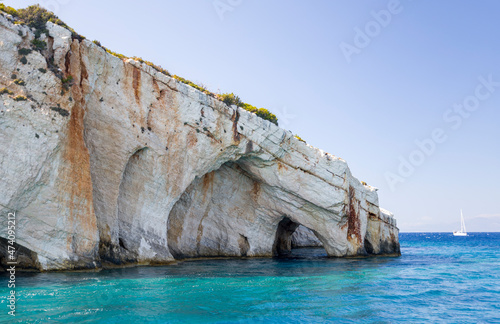 Cave in the rocky island cape in turquoise sea water with a yacht and mountains on horison and a cloud on the blue sky