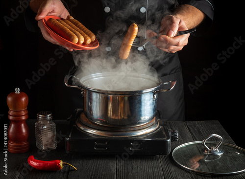 Chef cooks Vienna sausage in a saucepan. Working environment in the restaurant kitchen. Delicious breakfast or dinner photo