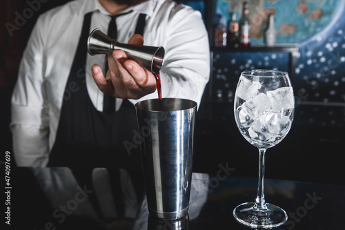 The hands of a professional bartender pour syrup into a measuring glass of jigger in a metal tool for preparing and stirring alcoholic cocktails of shaker drinks, and glasses with ice cubes photo
