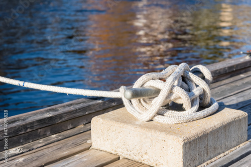 Close up of a mooring rope knotted to a cleat on a wooden pier in a harbour on a sunny autumn day. Selective focus. © alpegor