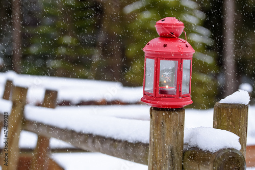 Close up of a red Christmas lantern on a snow covered wooden fence on a snowing winter day. Christmas decorations.