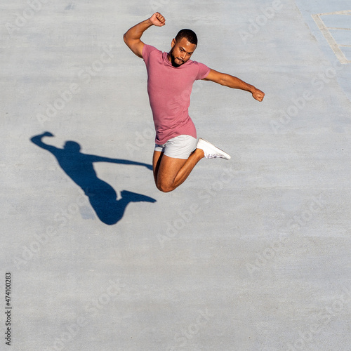 Multi-racial athletic male jumping with high energy and gray background.