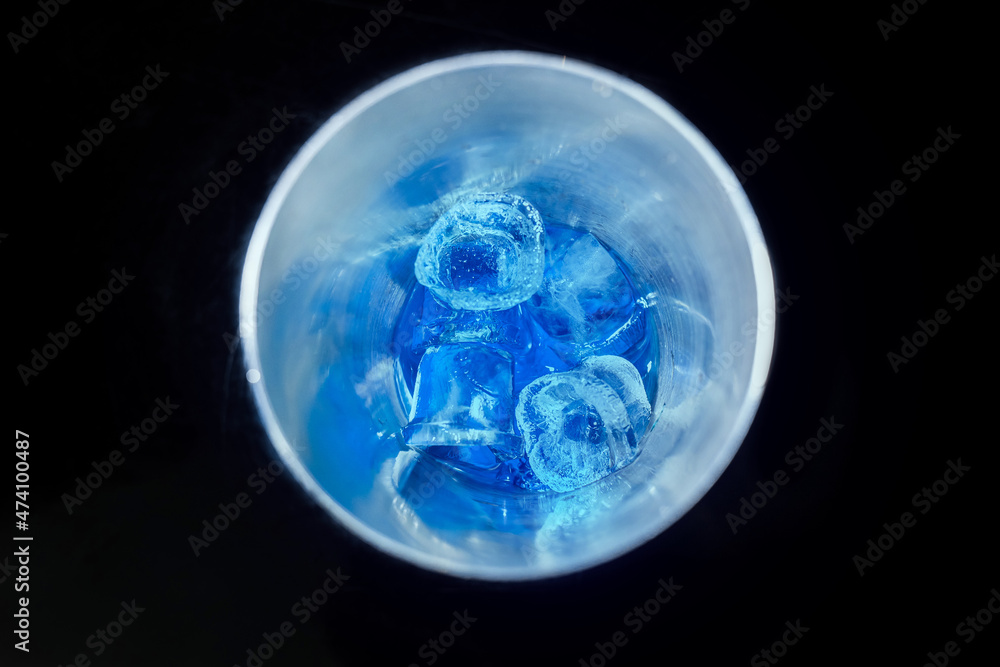 Blue cold syrup with ice in a tool for mixing and making alcoholic cocktails shaker on a black background, close-up Blue cold syrup with ice in a tool for mixing and making alcoholic cocktails shaker on a black background, close-up
