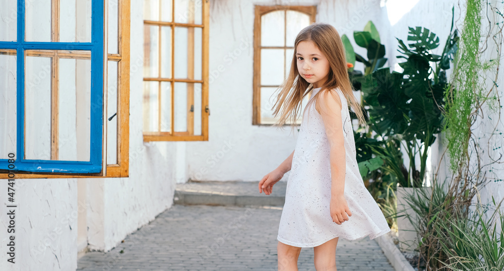 Fototapeta premium Beautiful girl with long hair in a white sundress in a light Balinese courtyard Greece Santorini vacation