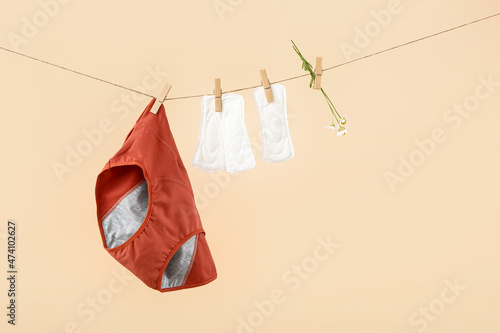 Period panties, pads and chamomile flowers hanging on rope against color background