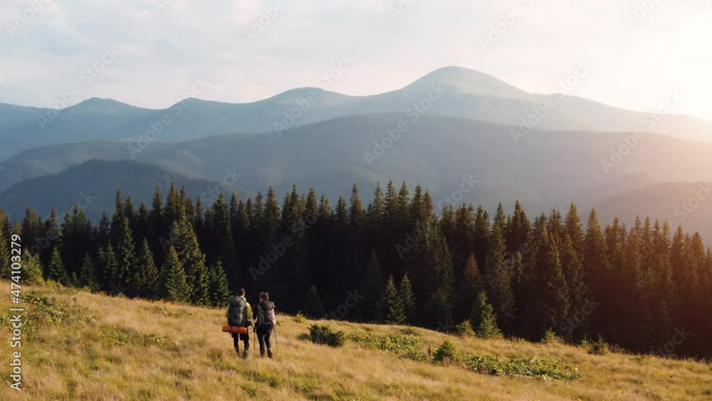 Couple of tourists walks down on hill. Majestic Carpathian Mountains. Beautiful landscape of untouched nature Couple of tourists walks down on hill. Majestic Carpathian Mountains. Beautiful landscape of untouched nature