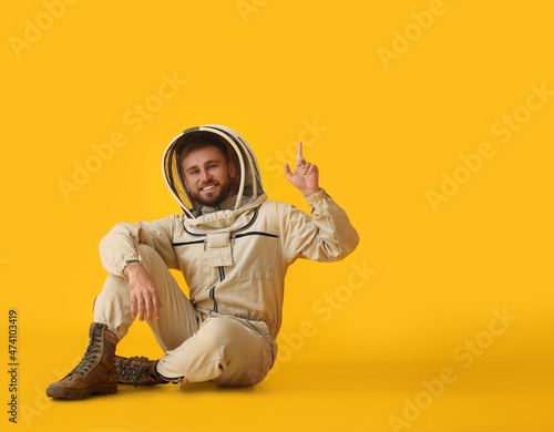 Male beekeeper in protective suit pointing at something on yellow background photo