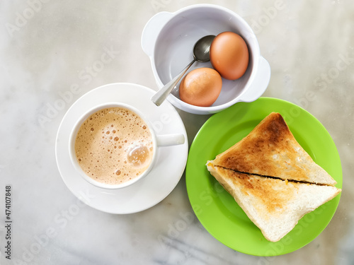 Popular Malaysian breakfast set. Milk tea or teh tarik, half boiled eggs and kaya butter toast set. photo
