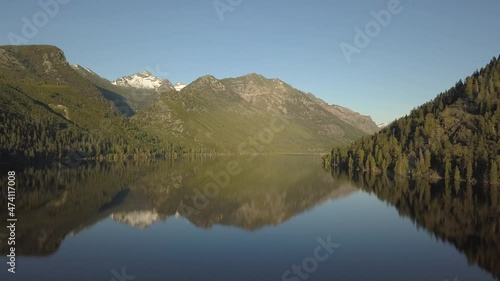 Smooth mountain lake with snowy peak behind pine forest  photo