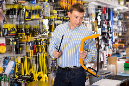 Confident glad man is choosing hacksaw in tools store photo