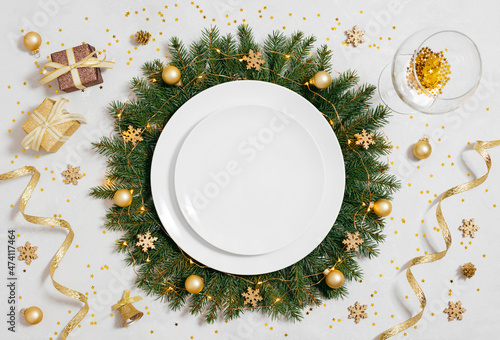 Christmas table setting with empty white plate and gold decorations on gray table. Copy space, top view, flat lay.