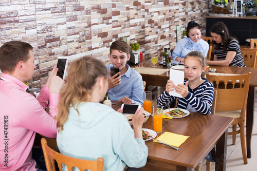 Parents with teenage children having dinner in family cafe and phubbing