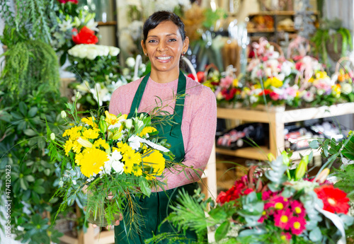Positive mexican female florist in apron holding composition from natural flowers at flower shop © JackF