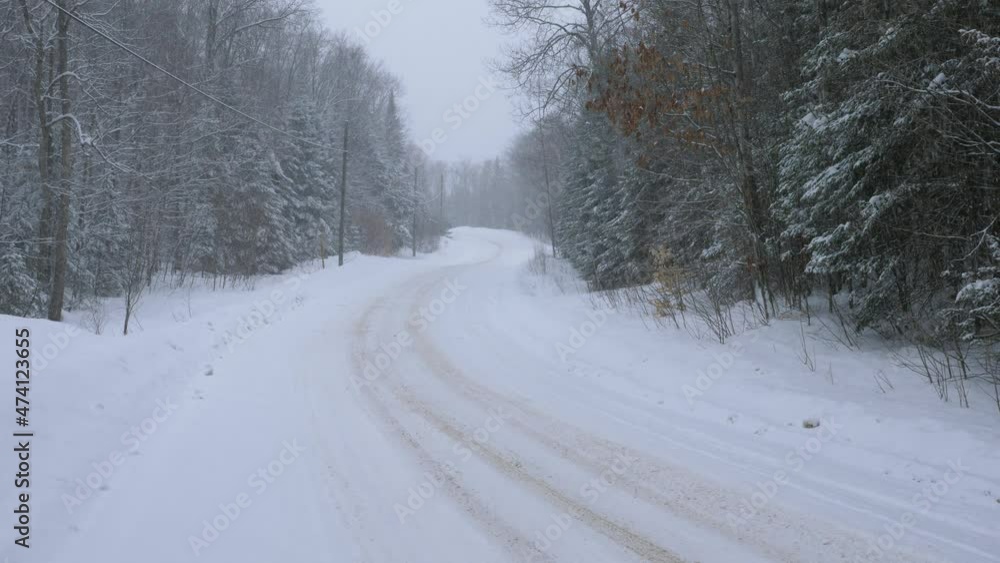 Curvy rural snow-covered winter road. Snow falling. Haliburton, Ontario, Canada. Tripod shot. 