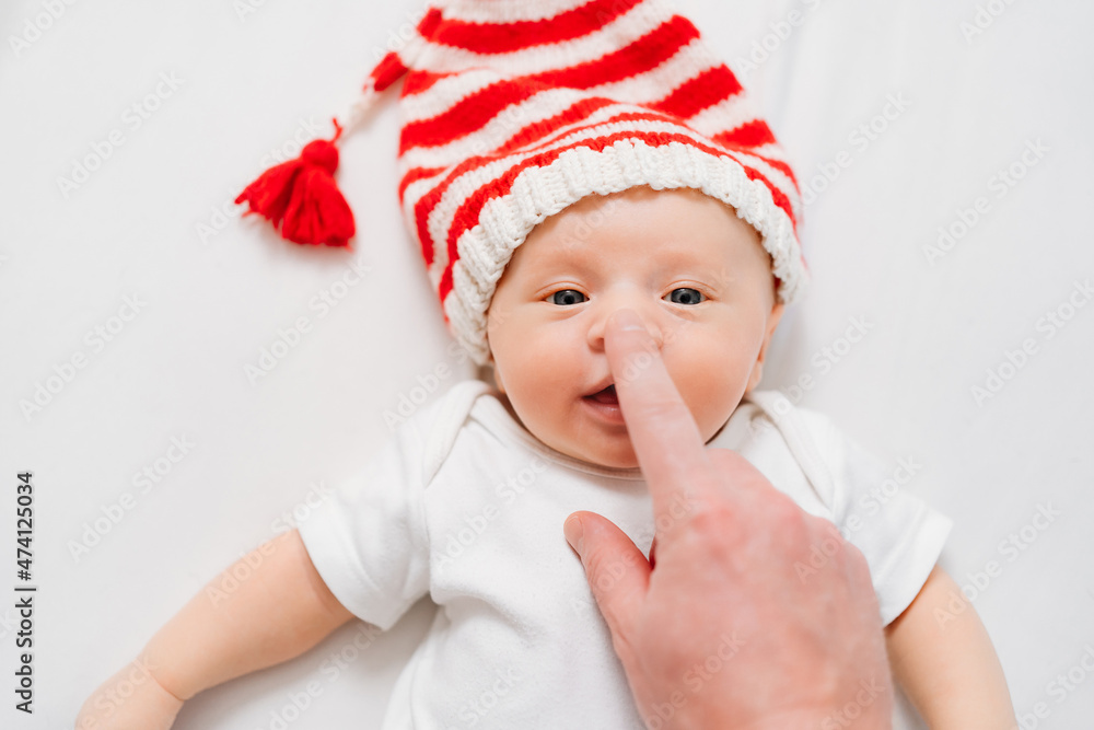 hand touches face of cute little kid in cap of Christmas elf or gnome.baby santa hand touches face of cute little kid in cap of Christmas elf or gnome.baby santa