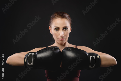 Caucasian woman boxer in sportswear and boxing gloves stands in a fighting stance and looks into the camera. Against a dark background. Strong woman's female fights